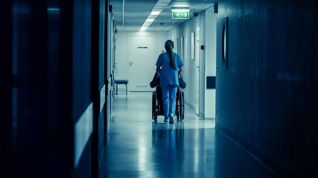Clinician in blue scrubs reviewing a chart in a hospital hallway